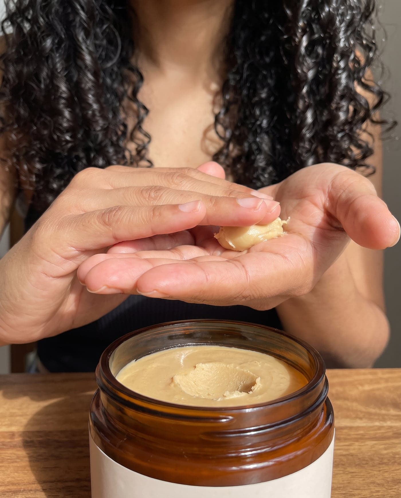 Hände wärmen eine Portion Batana-Creme über dem offenen Tiegel